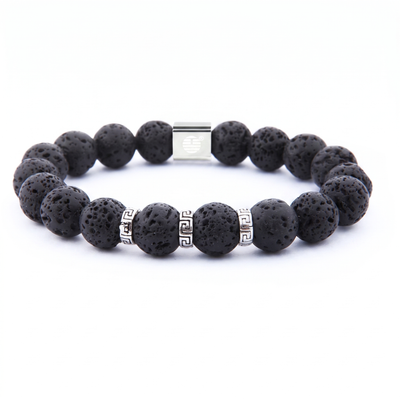 A beaded stretch bracelet made of black porous lava stone beads, accented with silver-tone spacer beads featuring a Greek key pattern and a rectangular silver clasp, shown on a plain white background.