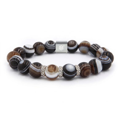 A beaded stretch bracelet featuring polished round beads with natural agate-like banding in black, white, brown, and gray, accented by a central silver-toned square bead and Greek key pattern spacers.