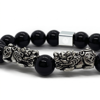 A close-up of a beaded bracelet featuring glossy black round beads, detailed silver-tone dragon charms, and a square silver magnetic clasp on a white background.