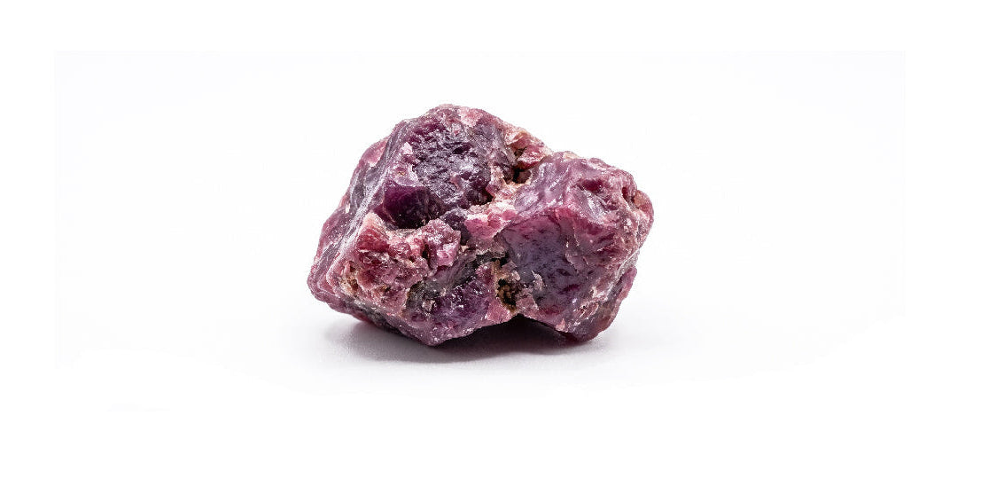 A rough, unpolished piece of dark purple crystal or mineral with a textured, porous surface, isolated on a solid white background.